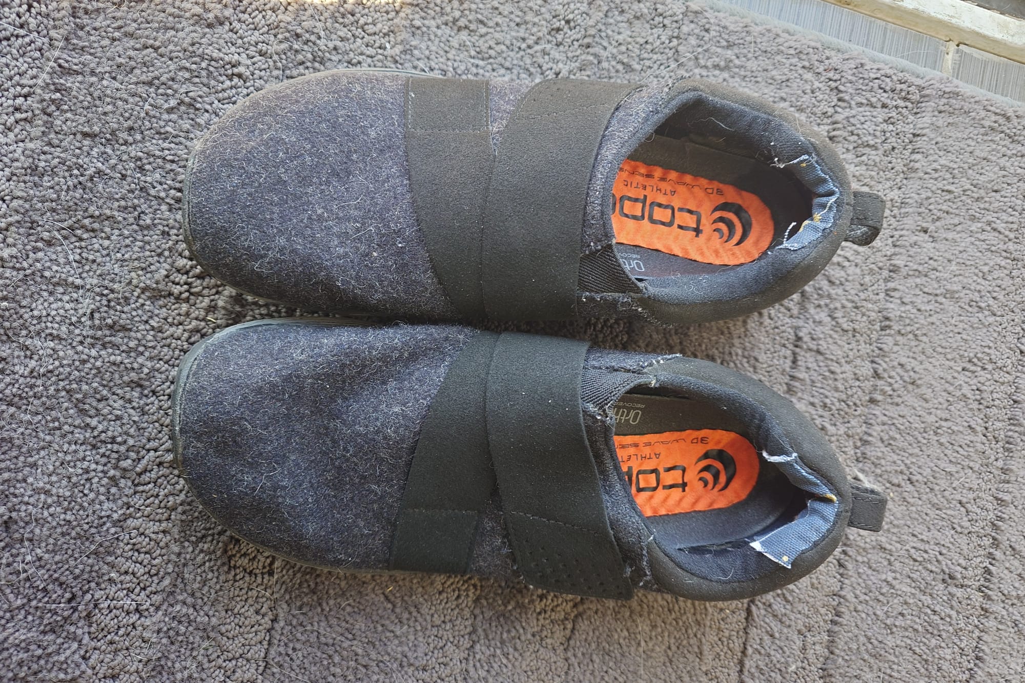 Top view of black shoes on carpet, repaired area of heel visible.