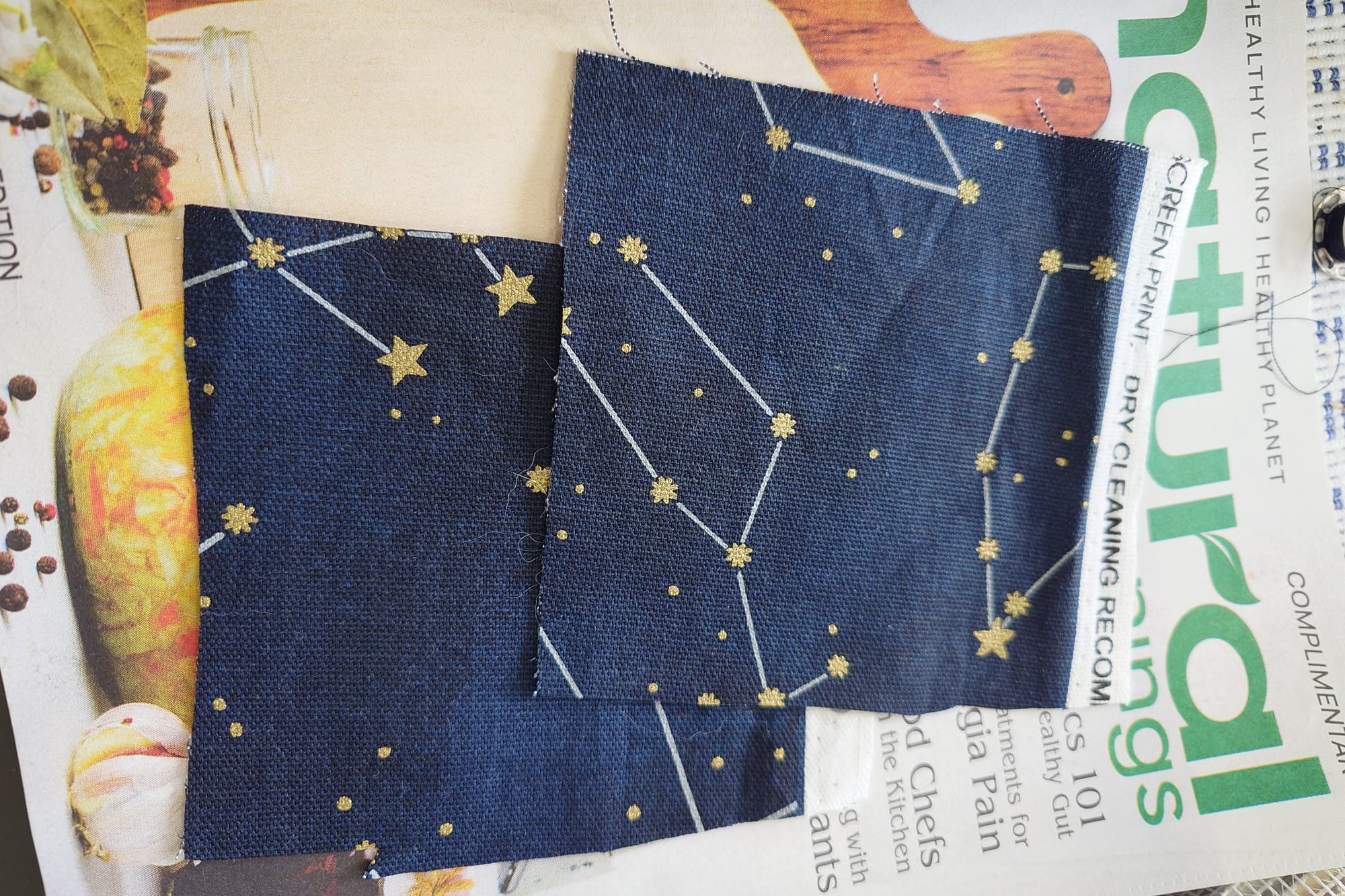 Two small pieces of dark blue fabric with illustrated constellations on a magazine.