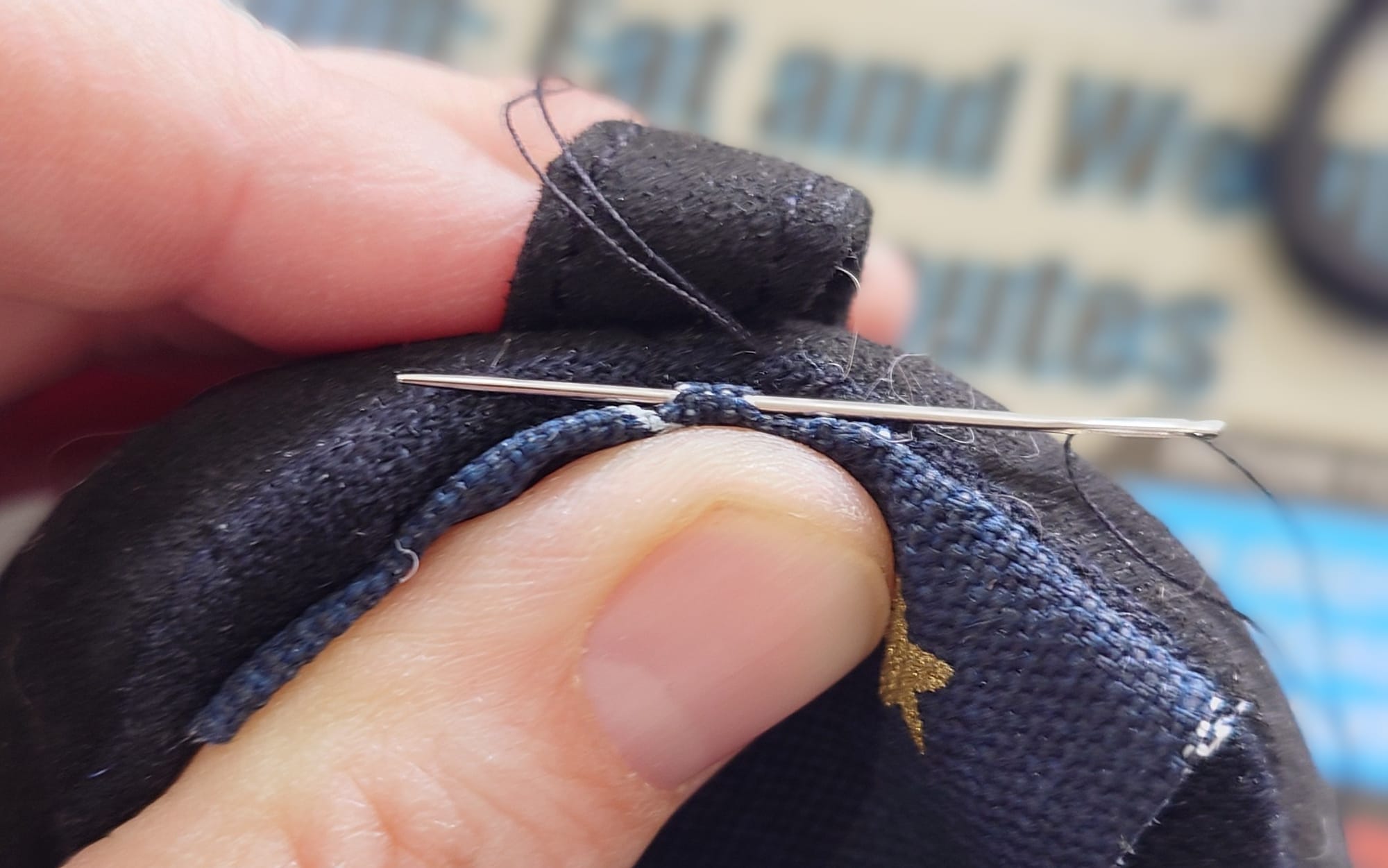 Closeup of a piece of fabric being sewn into the heel of a shoe. A needle and thread are visible, as are a person's hand.
