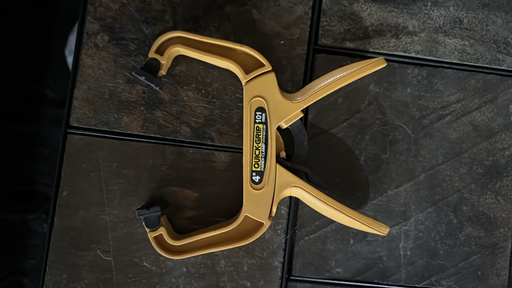 Yellow quick-grip clamp on stone tiled background.